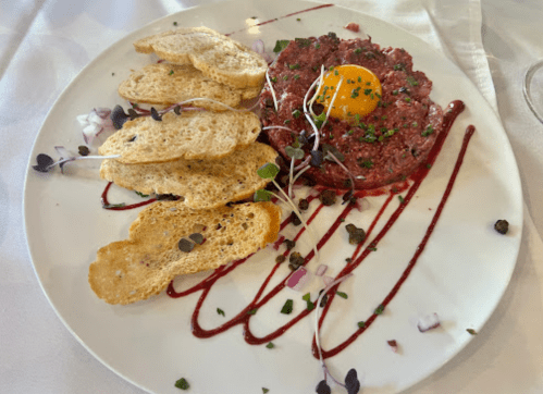 A plate of steak tartare topped with an egg yolk, served with toasted bread and garnished with herbs and sauce.