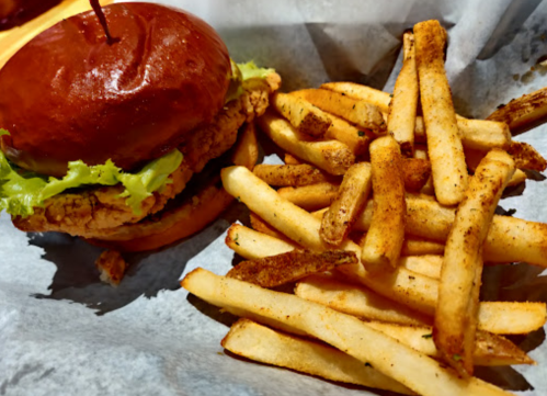 A crispy chicken sandwich with lettuce on a brioche bun, served with a side of seasoned French fries.
