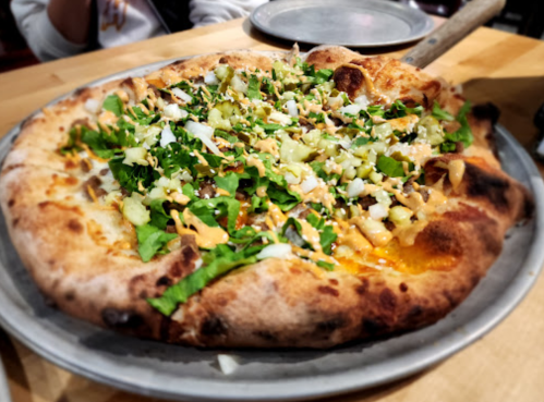A freshly baked pizza topped with lettuce, celery, and drizzled with sauce, served on a metal plate.