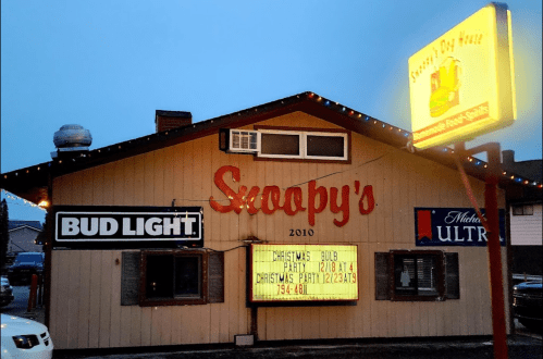 A cozy bar named Snoopy's with festive lights, featuring Bud Light signage and a Christmas party announcement.