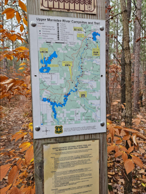 Map of Upper Manistee River campsites and trail, surrounded by autumn foliage in a forested area.