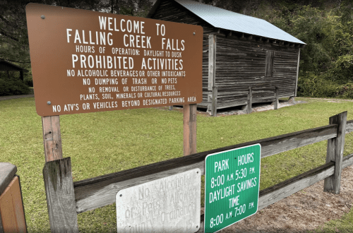 Sign at Falling Creek Falls detailing park hours and prohibited activities, with a rustic building in the background.