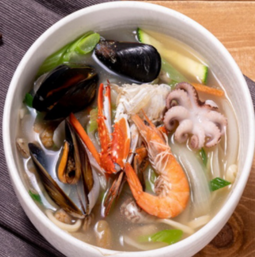 A bowl of seafood soup with shrimp, mussels, octopus, and vegetables in a clear broth.