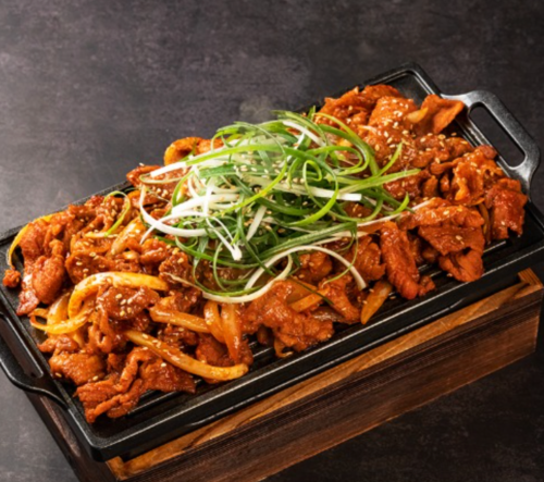 Sizzling platter of marinated meat with onions and green onions, garnished with sesame seeds.
