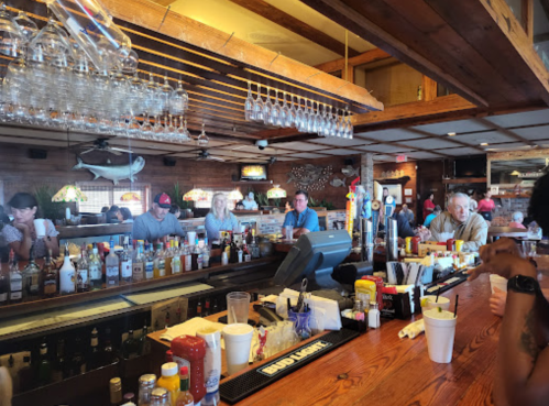 A lively bar scene with patrons enjoying drinks, surrounded by wooden decor and shelves of liquor bottles.