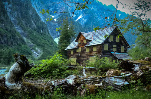 A rustic wooden cabin surrounded by lush greenery and mountains, with a serene atmosphere and a hint of snow on peaks.