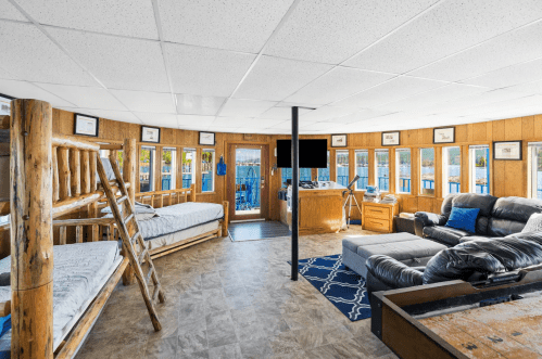 Cozy interior of a cabin with bunk beds, a sofa, and large windows overlooking a lake.