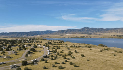 Aerial view of a scenic landscape with a river, mountains, and RVs parked along a winding road.