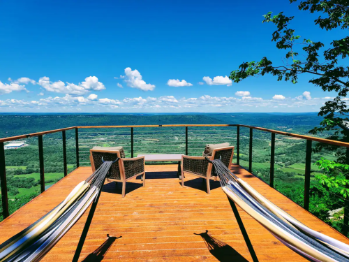 A scenic overlook with two hammocks and chairs, surrounded by lush greenery and a clear blue sky.