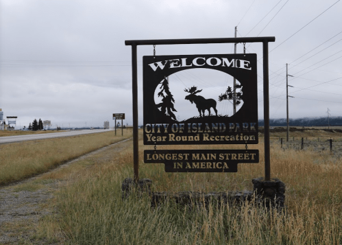Welcome sign for Island Park, highlighting year-round recreation and the longest main street in America, set against a cloudy sky.
