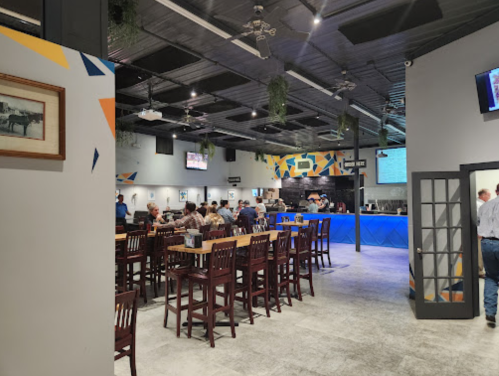 A spacious restaurant interior with patrons seated at high tables, a bar area, and colorful wall decor.