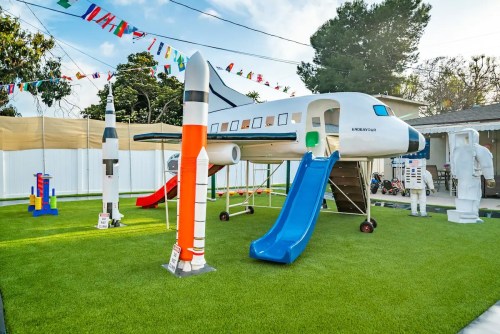 A colorful playground featuring a plane-shaped structure, slides, and rocket decorations on a grassy area.