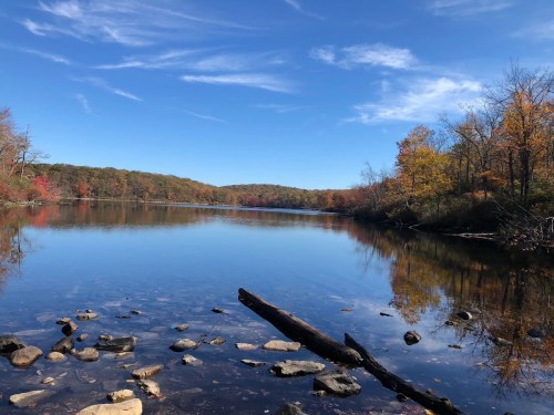 A serene lake surrounded by autumn foliage, reflecting a clear blue sky and colorful trees along the shore.