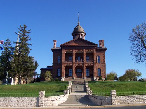 Historic brick building with a dome, flanked by trees and a clear blue sky, featuring a grand staircase leading up to it.