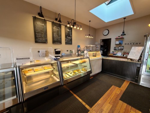 A cozy bakery interior featuring display cases with pastries, a chalkboard menu, and a skylight above.