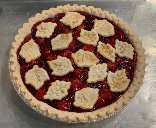 A cherry pie with a decorative crust featuring leaf-shaped cutouts on top, resting in a silver pie dish.