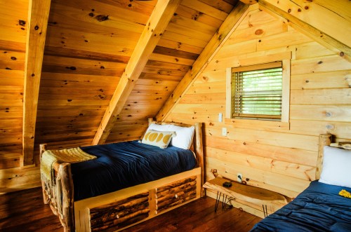 Cozy wooden cabin interior with two beds, sloped ceiling, and a small window, creating a warm, rustic atmosphere.