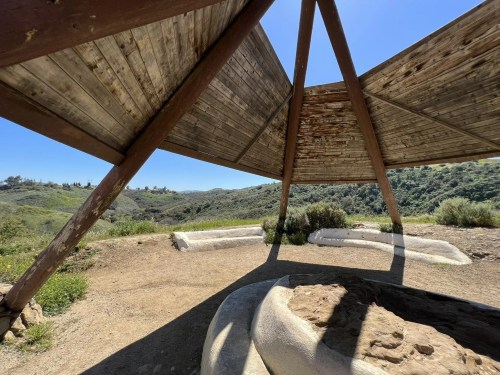 A wooden structure with a triangular roof overlooks a green hillside under a clear blue sky.