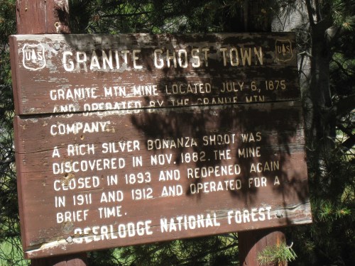 Sign for Granite Ghost Town, detailing its history and operation dates, set in a forested area.