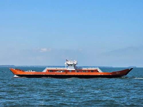 A large orange ferry boat sailing on calm blue waters under a clear sky.