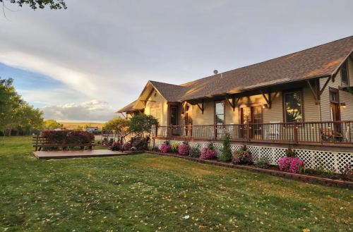A charming house with a porch, surrounded by colorful flowers and a green lawn under a cloudy sky.