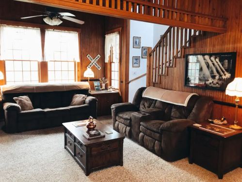 Cozy living room with brown sofas, a coffee table, and wooden accents, featuring large windows and a staircase.