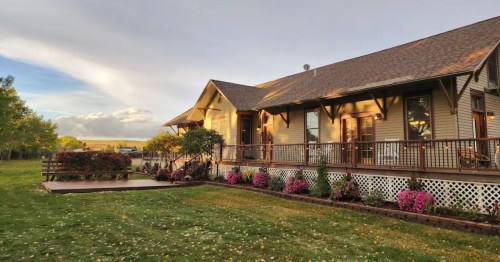 A charming house with a porch, surrounded by colorful flowers and a green lawn under a partly cloudy sky.