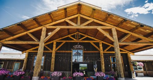 A rustic wooden building with a large overhang, adorned with flowers and string lights, under a blue sky.