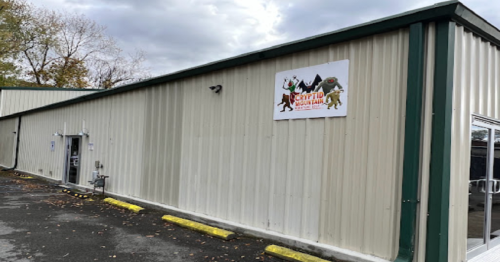 Exterior of a metal building with a sign for "Cryptid Mountain" featuring cartoon creatures, surrounded by a parking area.