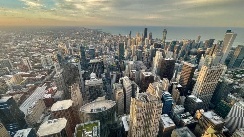 Aerial view of a sprawling city skyline with skyscrapers and a glimpse of the coastline under a cloudy sky.