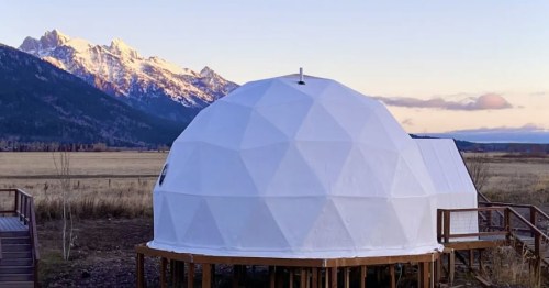 A geodesic dome structure on a wooden deck, set against a backdrop of mountains and a clear sky.