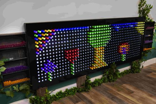 A colorful wall display made of vibrant, illuminated pegs arranged in patterns of flowers and trees.