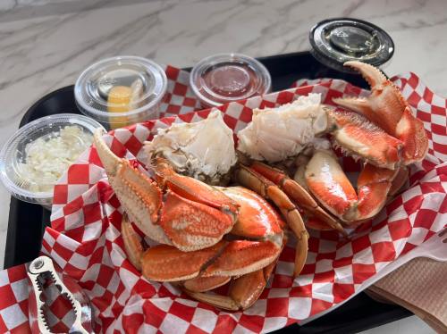 A tray with steamed crab legs, crab meat, and dipping sauces, served on red and white checkered paper.