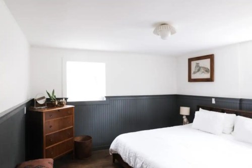 A cozy bedroom with a double bed, wooden dresser, and a framed artwork on the wall, featuring white and dark gray decor.
