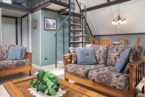 Cozy living area with patterned sofas, a wooden coffee table, and a spiral staircase leading to a loft.