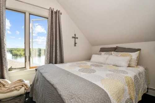 Cozy bedroom with a bed, decorative pillows, and a window overlooking a scenic view of water and trees.
