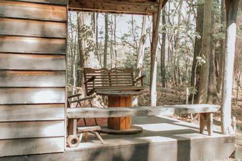 A rustic wooden cabin porch with a round table and two chairs, surrounded by trees in a serene forest setting.