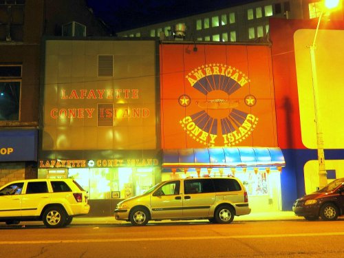 Nighttime view of Lafayette Coney Island and American Coney Island restaurants, with colorful signage and parked cars.