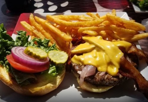 A juicy cheeseburger with bacon, lettuce, tomato, pickles, and a side of crispy fries on a white plate.