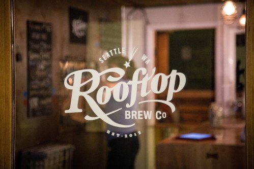 Logo of Rooftop Brew Co, located in Seattle, WA, established in 2012, seen on a glass door.