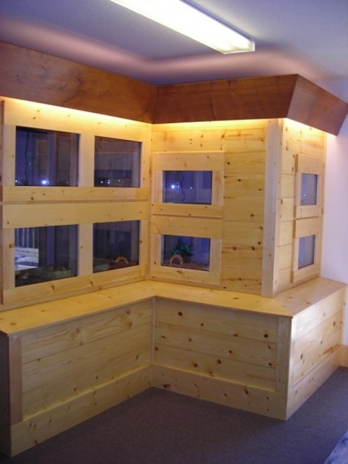 A wooden corner display unit with multiple glass windows, illuminated by soft lighting.