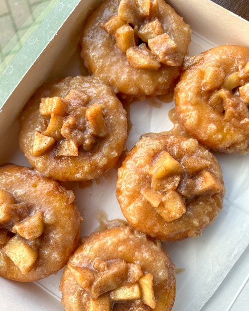 A box of six glazed donuts topped with caramelized apple pieces.