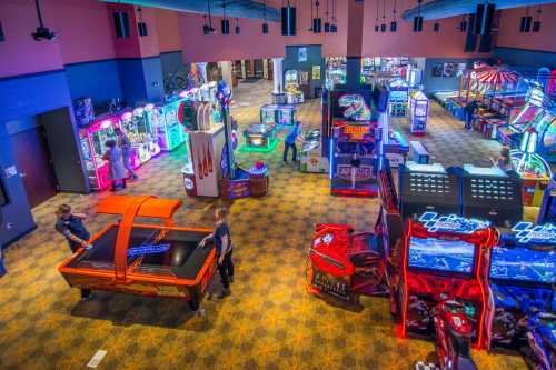 A vibrant arcade filled with colorful games and attractions, featuring people enjoying various activities.