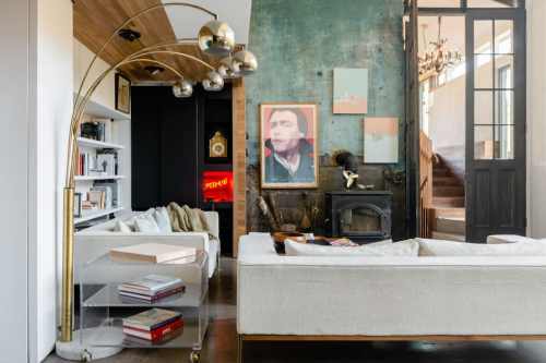 A stylish living room featuring a modern arc lamp, cozy sofas, artwork, and a fireplace against a textured green wall.