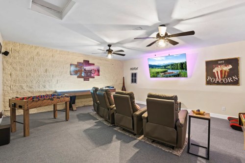 A cozy entertainment room with recliners, a large TV, game table, and popcorn sign on the wall.