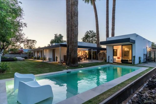 Modern home with a pool, surrounded by palm trees and a landscaped yard, at dusk.