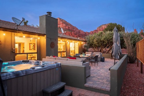 A cozy outdoor patio with a hot tub, seating area, and scenic red rock views at dusk.