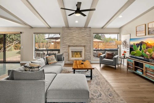 Modern living room with a gray sectional sofa, wooden coffee table, stone fireplace, and large windows.