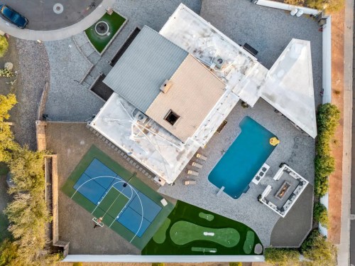 Aerial view of a modern home with a pool, basketball court, and putting green surrounded by gravel landscaping.