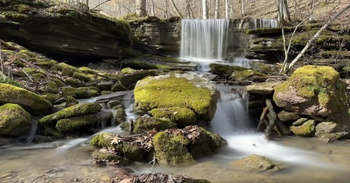 A serene waterfall cascades over moss-covered rocks in a tranquil forest setting.
